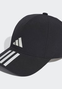 Gorra negra con una textura suave, con un visera curva, tres rayas blancas en la visera y un logotipo estilizado en el lado.