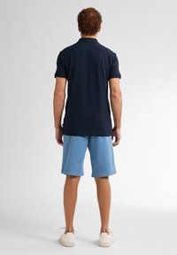 Marinblå polo skjorta med korta ärmar, kombinerad med ljusblå shorts. Shortsen har en avslappnad passform och sidofickor. Avslappnade vita sneakers.