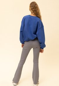 Blauwe oversized sweater gecombineerd met wijde, getekende broek met een geometrisch patroon in marineblauw en roze op een lichte achtergrond.
