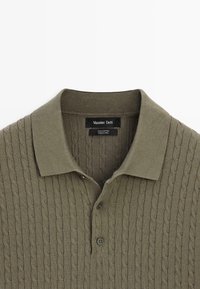 Olijfgroen polohemd gemaakt van 100% katoen, met een getextureerd kabelgebreid patroon, een kraag en een sluiting met twee knopen bij de hals.