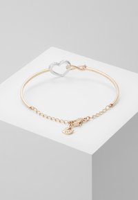 Gold-tone bracelet with a silver heart clasp and a small heart charm. Features a linked chain extender for adjustable sizing.