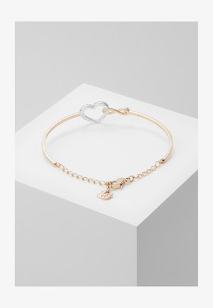 Zlato tonirana zapestnica s srebrnim srčastim zapenjalom in majhnim srčkom. Ima povezano verigo za podaljšanje, ki omogoča prilagodljivo velikost.