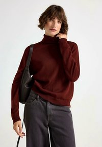 Bourgogne rullekrave trøje lavet af strikket stof, med lange ærmer og en afslappet pasform, kombineret med højtaljede sorte jeans og en tekstureret taske.