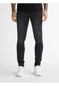 Black skinny jeans with a smooth texture and minimal fading. Worn with white sneakers, showcasing a streamlined fit and clean design.