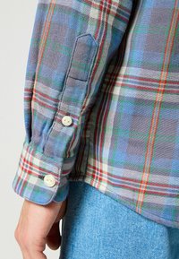 Camisa de franela de cuadros multicolores con grandes patrones de cuadros en azul, verde, rojo y blanco, con puños abotonados y una textura suave.