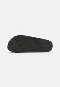 Talpă din cauciuc negru cu textură în zigzag, având o formă rotundă, o ușoară curbură la călcâi și detalii de design minime.