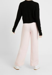 Czarny krótki sweter z prążkowanym wykończeniem, zestawiony z jasnoróżowymi spodniami o szerokich nogawkach z teksturowanej tkaniny. Model kończy look białymi butami.