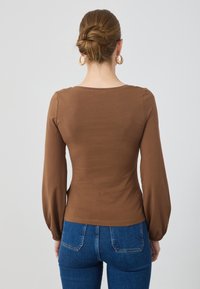 Braunes Langarmshirt mit taillierter Passform und puffy Ärmeln, kombiniert mit blauen Jeans aus Denim, die eine glatte Stofftextur zeigen.