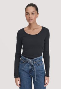 Zwarte long sleeve top met een ronde hals, gecombineerd met high-waisted blauwe jeans met een gespen taille en subtiele stiksels.