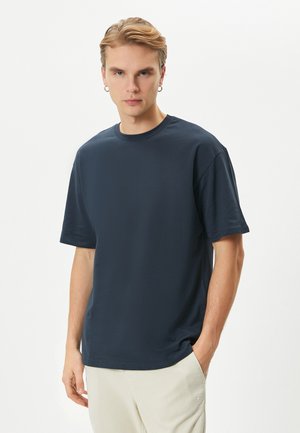 Camiseta de algodón azul marino con mangas cortas, cuello redondo y corte holgado. Presenta una textura suave y un sutil detalle del logo en el dobladillo.