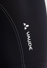 Shorts en tissu extensible noir avec des coutures blanches et un logo "VAUDE" visible sur le côté gauche. Texture lisse, design athlétique.