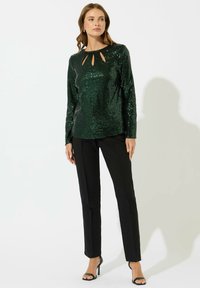 Top verde con paillettes a maniche lunghe con aperture sul collo, abbinato a pantaloni neri a gamba dritta e tacchi a spillo neri.