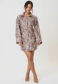 Rochie cămașă cu imprimeu de zebră în tonuri de brun și crem, având guler, închidere cu nasturi și mâneci lungi. Textură de țesătură netedă.