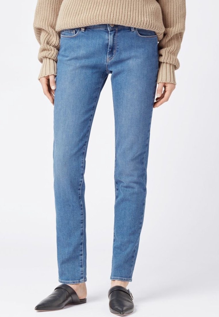 Skinny blue jeans with a smooth denim texture, five-pocket design, and slight fraying at the hem, paired with black slip-on shoes.