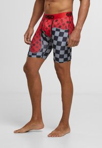 Shorts de sport à motif rouge et noir avec un design en damier, taille élastique et coupe ajustée. Fabriqués en matière extensible.