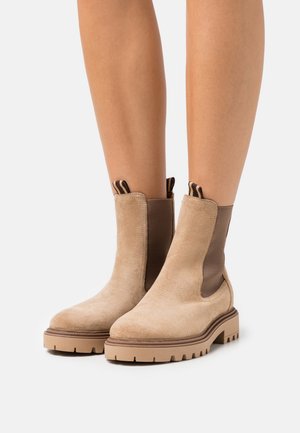 Bottines en daim beige avec des empiècements élastiques marron sur les côtés et des languettes pour les enfiler. Semelles en caoutchouc épaisses avec une profonde bande de roulement pour une meilleure adhérence.