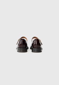 Zapatos de cuero pulido marrón con punta redondeada, dos hebillas y un tacón bajo de goma negra. Textura suave, diseño minimalista.