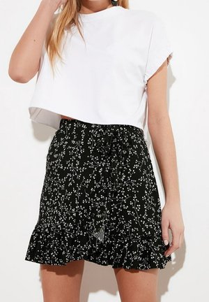 Vrouw die een wit cropped t-shirt en een zwarte rok draagt met kleine witte bloempatronen en een gerimpelde zoom.
