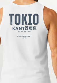 White tank top featuring large graphic text "TOKIO KANTŌ" in gray with Japanese characters, coordinates, and brand name "NEVERLESS®" below.