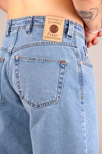 Light blue denim jeans featuring a leather brand patch on the waistband, copper rivets, and two back pockets. Classic five-pocket design.