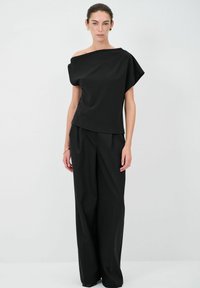 Top nero senza spalline con design drappeggiato, abbinato a pantaloni neri a gamba larga. Tessuto liscio con silhouette minimalista e senza motivi visibili.