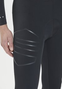Figurbetonte schwarze Leggings mit glatter Textur und gummiartigen geometrischen Akzenten am Oberschenkel, die für Leistung und Komfort entworfen wurden.