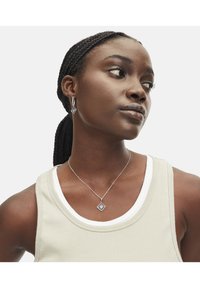 Zilveren sieradenset met een diamanten hanger en bijpassende oorbellen. Draagt over een geribbelde, lichtgekleurde tanktop.