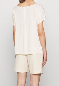 Top leggero beige, dalla vestibilità ampia, con scollatura rotonda e maniche corte. Presenta una cucitura centrale sul retro e una texture liscia. Abbinato a pantaloni corti beige.