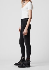 Svarta tajta jeans med hög midja, tillverkade av stretchig denim. Matchad med svarta snörda ankelstövlar och en vit figurnära topp.