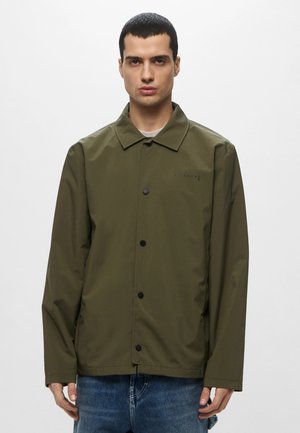 Giacca leggera color verde oliva, resistente all'acqua, con bottoni davanti, colletto a punta e logo discreto sopra il petto sinistro. Vestibilità casual.