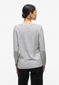 Pilkas megztinis ilgomis rankovėmis, plačiu iškirpimu ir ribštu kraštu. Švelnios tekstūros, laisvo silueto, be matomų raštų ar apdailos detalių.