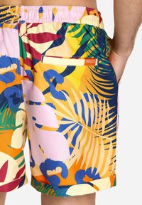 Men's swim shorts in bright orange, blue, pink, and green tropical print. Features an elastic waistband and a back pocket with logo tag.