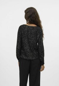 Maglione nero dal taglio morbido, con un motivo a macchie, maniche lunghe e colletto ampio. Abbinato a pantaloni neri fluidi.