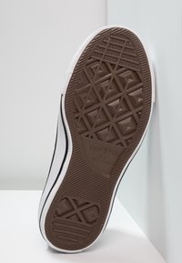 Semelle d'une chaussure blanche Converse All Star avec une bande de roulement géométrique distinctive en gomme marron.