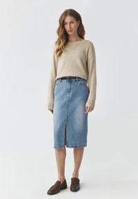 Beige gebreide trui, lichtblauwe denim midi-rok met voorkleur, en donkerbruine instap schoenen. Eenvoudige en casual outfit.