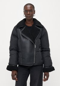 Giacca a vento nera con colletto e polsini in shearling, dotata di un design trapuntato e di una cerniera asimmetrica. Realizzata in un materiale liscio e lucido.