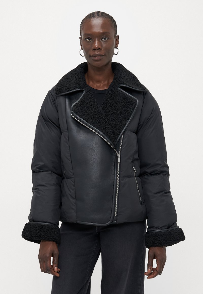 Svart pufferjakke med en shearling-krage og -mansjetter, med et quiltet design og asymmetrisk glidelås. Laget av et glatt, blankt materiale.