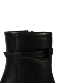 Bottine en cuir noir à finition lisse, fermeture zippée et sangle décorative à boucle autour de la cheville.