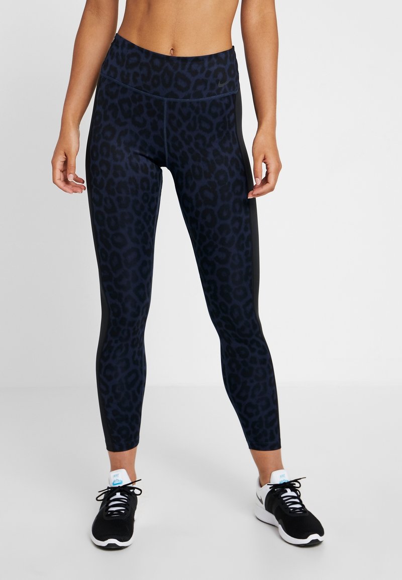 Leggings neri con un motivo a stampa leopardo blu scuro, vita alta e tessuto texturizzato. Abbinati a scarpe sportive bianche e nere.
