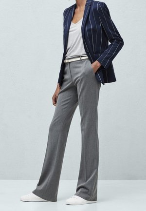 Granatowa marynarka w paski na szarym t-shircie, zestawiona z szerokimi szarymi spodniami i białymi sneakersami. Miękki materiał o dopasowanym kroju.