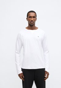 Λευκό βαμβακερό μπλουζάκι με μακριά μανίκια, στρογγυλή λαιμόκοψη και μικρό λογότυπο στο στήθος. Διαθέτει άνετη εφαρμογή και απαλό ύφασμα.