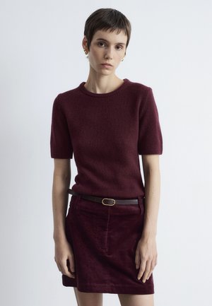 Burgundy short-sleeve sweater in soft texture, paired with a matching corduroy skirt. Brown belt with a circular gold buckle accents the outfit.