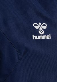 Marineblauwe sportstof heeft een gestructureerd patroon, met een witte "hummel"-logo en een kenmerkend bij-embleem erop gedrukt.