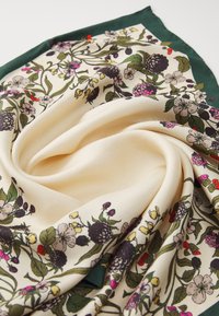 Écharpe en soie présentant un fond crème avec un motif floral vert, violet et rose, bordé d'un liseré vert foncé. Texturée et fluide.