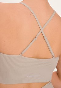 Hellgrauer, gerippter Sport-BH mit Kreuzträgern und verstellbarem Verschluss. Mit Logo am unteren Band. Weiche Textur und figurbetontes Design.