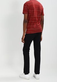 Punainen raidallinen lyhythihainen T-paita, mustat kapenevat housut ja valkoiset lenkkitossut. Sileä puuvillakuitu; paidassa olevat raidat vaihtelevat leveydeltään.