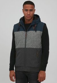 Die Weste mit Reißverschluss verfügt über ein farbblockiertes Design mit navyblauen, grauen und dunkelgrauen Paneelen. Texturierten Stoff mit verstellbarem Kapuzen und Taschen.