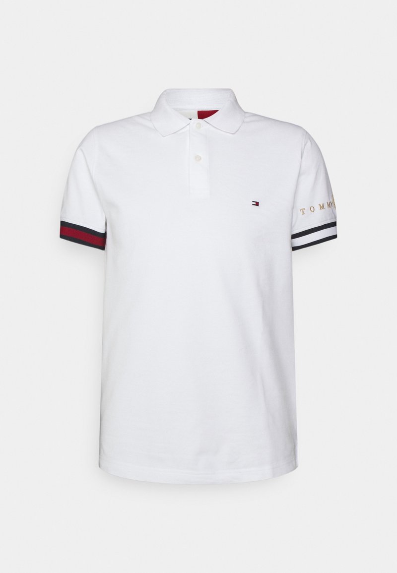 Polo shirt blanc en coton avec un col classique, trois boutons et des accents rayés bleu marine et rouge sur les manches. Broderie "TOMMY" en or.