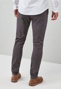 Szare spodnie dresowe o dopasowanym kroju, wykonane z tkaniny tkanej, z kieszeniami i w połączeniu z brązowymi zamszowymi botkami za kostkę.