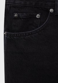 Jean en denim noir avec poche avant, rivets métalliques et coutures visibles sur tissu texturé.